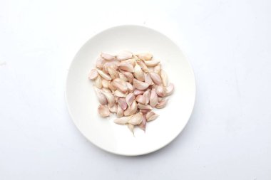 Beyaz arkaplanda izole edilmiş beyaz seramik tabakta taze çiğ sarımsak karanfilleri.