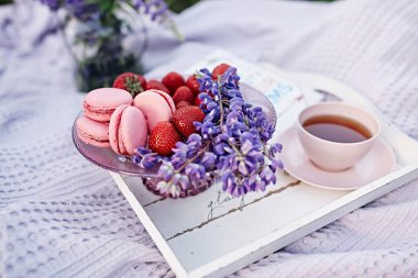 Beautiful summer breakfast. Pink macaroons, strawberry and tea with lupine flowers. Nice day. Pink cup of tea. 