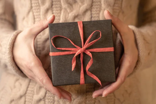 Kahverengi kağıda sarılı bir hediye kutusu ve kırmızı kurdeleyle bağlanmış bir kadın elinde, yakın plan.