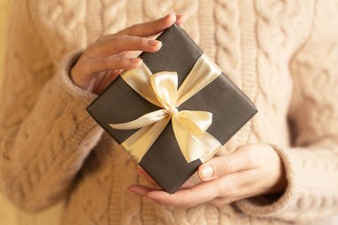 Kahverengi kağıda sarılı ve altın kurdeleyle bağlanmış bir kutu, kadınların elinde, yakın plan.