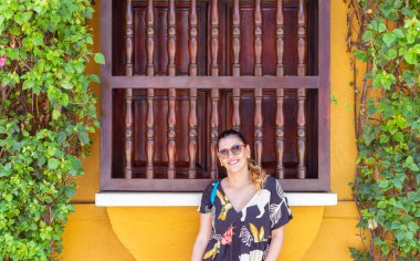 Eski ahşap bir pencerenin önünde poz veren Latin kadın.