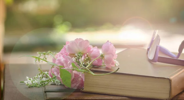 Close-up de livro, copos e flores em fundo bokeh embaçado. Lazer, natureza, estilo de vida e conceito de relaxamento. Dupla exposição. pequenas flores valerianas brancas e botões de rosa — Fotografia de Stock