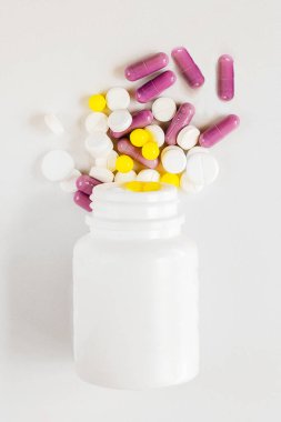 Beyaz bir zemin üzerinde çeşitli tablet ve kapsülleri, arkasında bulanıklık olan kapsüllerle tedavi eder