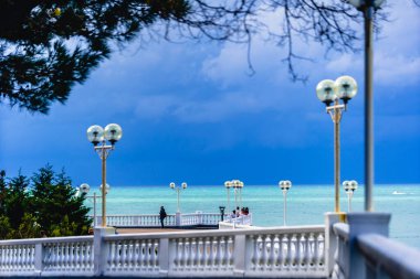 Sonbaharda tatil köyünün seti. Balyoz ve sayısız fenerle dolgu seti. Yeşil bir deniz ve karanlık, fırtınalı bir gökyüzü. İnsanlar set boyunca yürür ve denize bakarlar. Gelendzhik tatil beldesi, Karadeniz