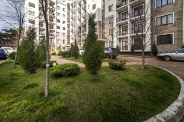 Çok katlı bir binanın geniş kıvrımlı balkonunda metal, siyah, desenli demir parmaklıklar var. Balkon konut kompleksinin, dağların ve bulutların evlerinin manzarasını sunuyor..