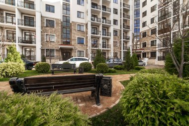 Çok katlı bir binanın geniş kıvrımlı balkonunda metal, siyah, desenli demir parmaklıklar var. Balkon konut kompleksinin, dağların ve bulutların evlerinin manzarasını sunuyor..