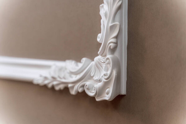The panel is a plaster frame with patterned corners on the wall of the room. Interior design. Loft with baroque elements. Beige-brown shades.