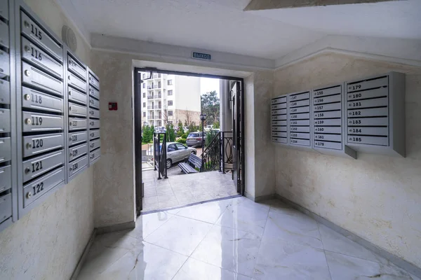 çok katlı yeni bir binanın girişinden çıkıyorlar. Girişteki posta kutuları..