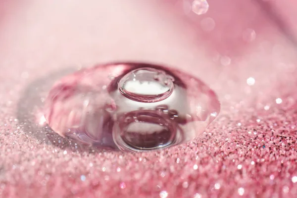 Ein Tropfen kosmetisches Gel auf einem rosa glänzenden Hintergrund. — Stockfoto