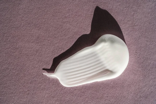 Mor arka planda beyaz krem lekesi. Kremin dokusu..