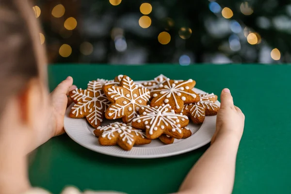 Zázvor vánoční sušenky v dětských rukou na pozadí vánočního stromečku. — Stock fotografie