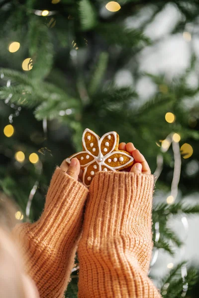 Biscotti di Natale allo zenzero nelle mani dei bambini sullo sfondo dell'albero di Natale. — Foto Stock