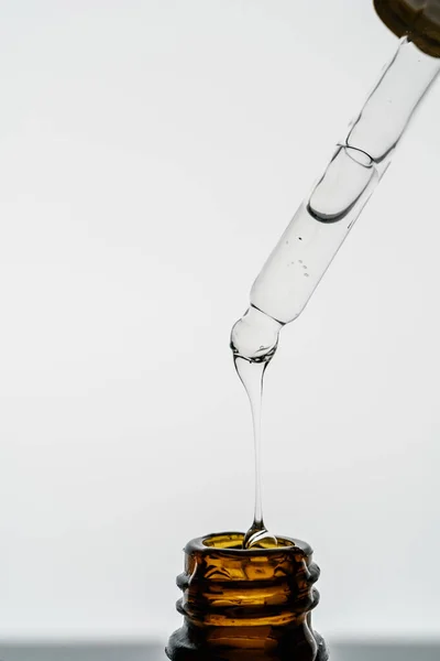 Pipeta transparente con cosméticos y botella sobre fondo claro. — Foto de Stock