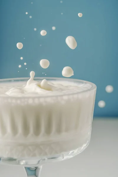 ミルクは青い背景に美しい結晶ガラスに注ぎ、周りに飛び散る. — ストック写真