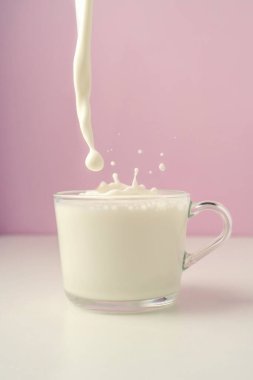 Mor arka planda şeffaf bir fincana süt dökülür..