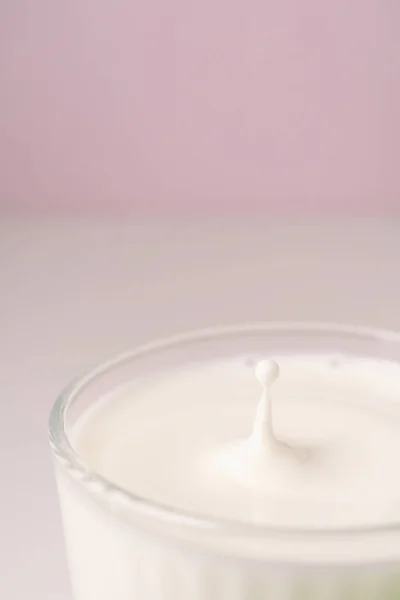 O leite goteja em um vidro facetado transparente. — Fotografia de Stock