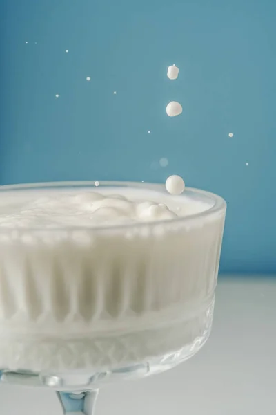 Mleko wlewa się do pięknej kryształowej szklanki na niebieskim tle i rozbryzga się wokół. — Zdjęcie stockowe