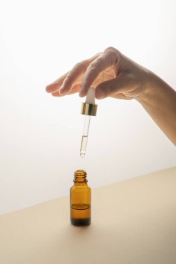 Şişenin üzerinde kozmetik ile pipeti tutan el..