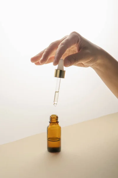 Şişenin üzerinde kozmetik ile pipeti tutan el..