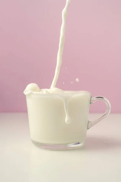 La leche se vierte en una taza transparente sobre un fondo púrpura. — Foto de Stock