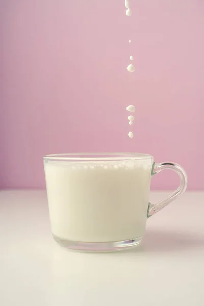 La leche se vierte en una taza transparente sobre un fondo púrpura. — Foto de Stock