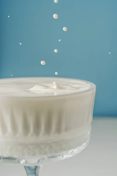 ミルクは青い背景に美しい結晶ガラスに注ぎ、周りに飛び散る. — ストック写真