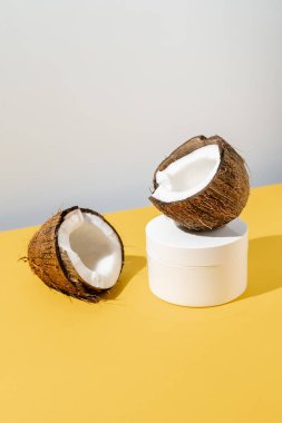 Sarı ve gri arka planda iki yarım hindistan cevizi ve bir kavanoz kozmetik..