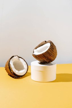 Sarı ve gri arka planda iki yarım hindistan cevizi ve bir kavanoz kozmetik..