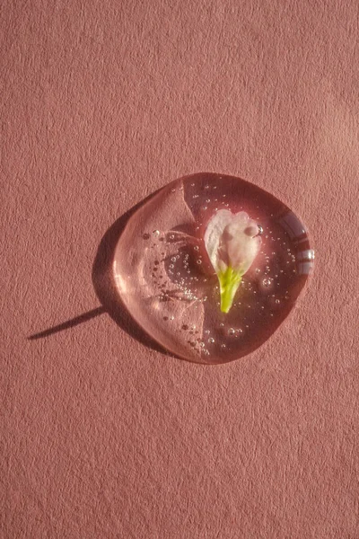 ピンクの背景に花を持つ化粧品ゲルのドロップ. — ストック写真