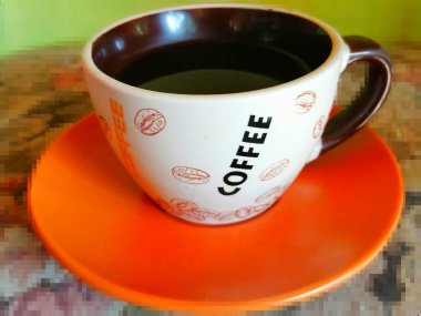 Kahve kupası. Üzerinde yazı olan parlak bir kupa ve turuncu bir fincan ve mozaik arka plan üzerine siyah damlatılmış kahve.. 