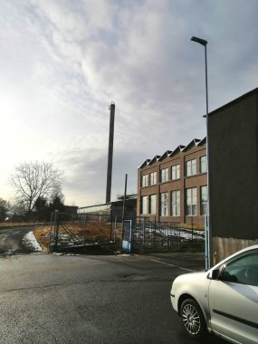 Fabrikanın üzerinde bulutlar var. Çitleri, kapısı, bacası ve arabası olan modern bir fabrikanın üzerinde yuvarlanan büyük bulutlar.. 