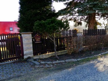 Posta kutusu. Bahçesi ve çeşitli ağaçları olan bir evin yakınındaki ahşap bir çitte asılı kahverengi bir posta kutusu.. 