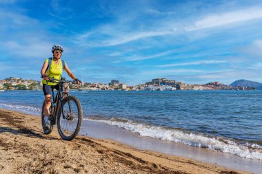 Toskana Takımadası 'ndaki Elba Adası' nda Akdeniz kıyısında, Porto Ferraio, Toskana, İtalya 'nın önünde elektrikli dağ bisikletine binen hoş bir kadın.