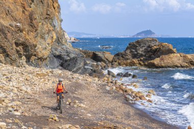 Akdeniz kıyısında, Toskana Takımadası, İtalya 'da Elba adasında gün batımında elektrikli dağ bisikleti süren hoş bir kadın.