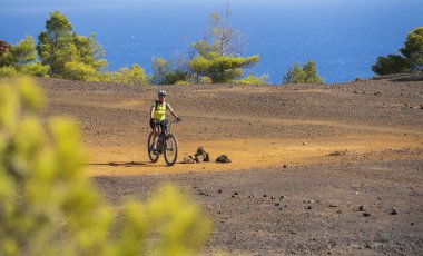 Akdeniz kıyısında, Toskana Takımadası, İtalya 'da Elba adasında gün batımında elektrikli dağ bisikleti süren hoş bir kadın.