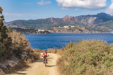 İtalya Toskana Takımadası 'ndaki Elba Adası' nda Akdeniz kıyısında elektrikli dağ bisikletine binen hoş bir kadın.