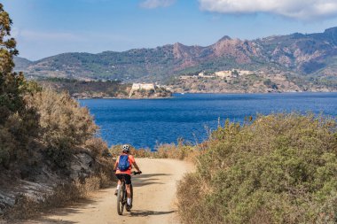 İtalya Toskana Takımadası 'ndaki Elba Adası' nda Akdeniz kıyısında elektrikli dağ bisikletine binen hoş bir kadın.