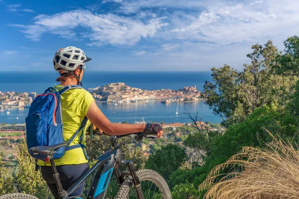 Toskana Takımadası 'ndaki Elba Adası' nda Akdeniz kıyısında, Porto Ferraio, Toskana, İtalya 'nın önünde elektrikli dağ bisikletine binen hoş bir kadın.