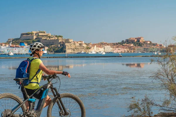 Toskana Takımadası 'ndaki Elba Adası' nda Akdeniz kıyısında, Porto Ferraio, Toskana, İtalya 'nın önünde elektrikli dağ bisikletine binen hoş bir kadın.