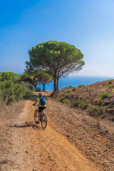 Akdeniz kıyısında, Toskana Takımadası, İtalya 'da Elba adasında gün batımında elektrikli dağ bisikleti süren hoş bir kadın.
