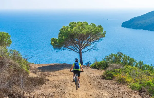 Akdeniz kıyısında, Toskana Takımadası, İtalya 'da Elba adasında gün batımında elektrikli dağ bisikleti süren hoş bir kadın.