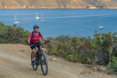 İtalya Toskana Takımadası 'ndaki Elba Adası' nda Akdeniz kıyısında elektrikli dağ bisikletine binen hoş bir kadın.