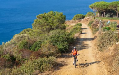 İtalya Toskana Takımadası 'ndaki Elba Adası' nda Akdeniz kıyısında elektrikli dağ bisikletine binen hoş bir kadın.
