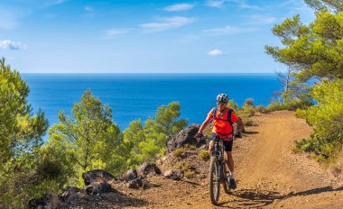 İtalya Toskana Takımadası 'ndaki Elba Adası' nda Akdeniz kıyısında elektrikli dağ bisikletine binen hoş bir kadın.