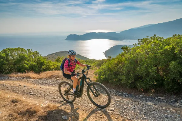 Akdeniz kıyısında, Toskana Takımadası, İtalya 'da Elba adasında gün batımında elektrikli dağ bisikleti süren hoş bir kadın.