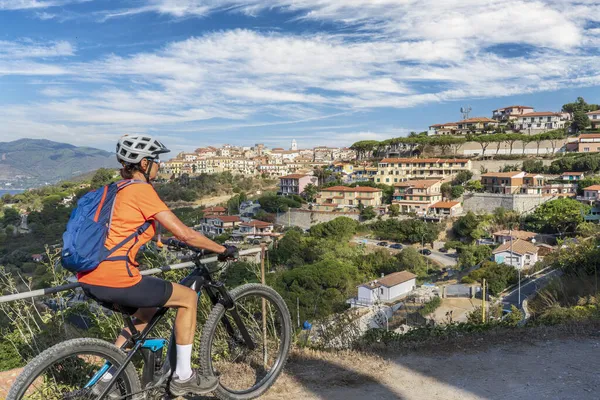 Toskana Takımadası 'ndaki Elba Adası' nda Akdeniz kıyısında, Capoliverie, Toskana, İtalya 'nın önündeki elektrikli dağ bisikletine binen hoş bir kadın.