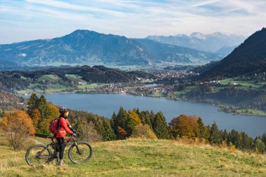 Alpsee Gölü 'nün manzarasının tadını çıkaran elektrikli dağ bisikletli hoş bir kadın Immenstadt, Bavyera Alpleri, Almanya' daki Allgaeu Alpleri 'nde atüminyum atmosferde.