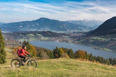 Alpsee Gölü 'nün manzarasının tadını çıkaran elektrikli dağ bisikletli hoş bir kadın Immenstadt, Bavyera Alpleri, Almanya' daki Allgaeu Alpleri 'nde atüminyum atmosferde.