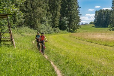 Elektrikli dağ bisikleti ve elektriksiz torunu olan büyükannesi Bavyera, Gemany 'deki Franconian İsviçre bölgesinde düzlük bir çayır yolunda elektriksiz.