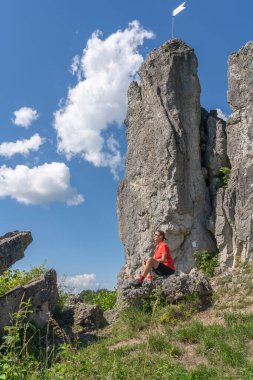 Franconian İsviçre 'de kayalık bir patikada, elektrikli dağ bisikleti üzerinde dinlenen yaşlı güzel bir kadın, ünlü kaya tepelerine hayran, Ağaç tepeleri, Bavyera, Almanya